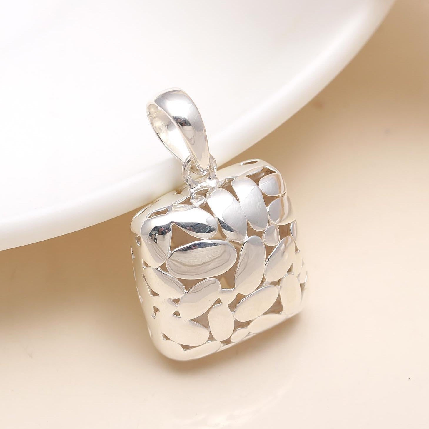 Silver pendant with leaf design on a beige surface