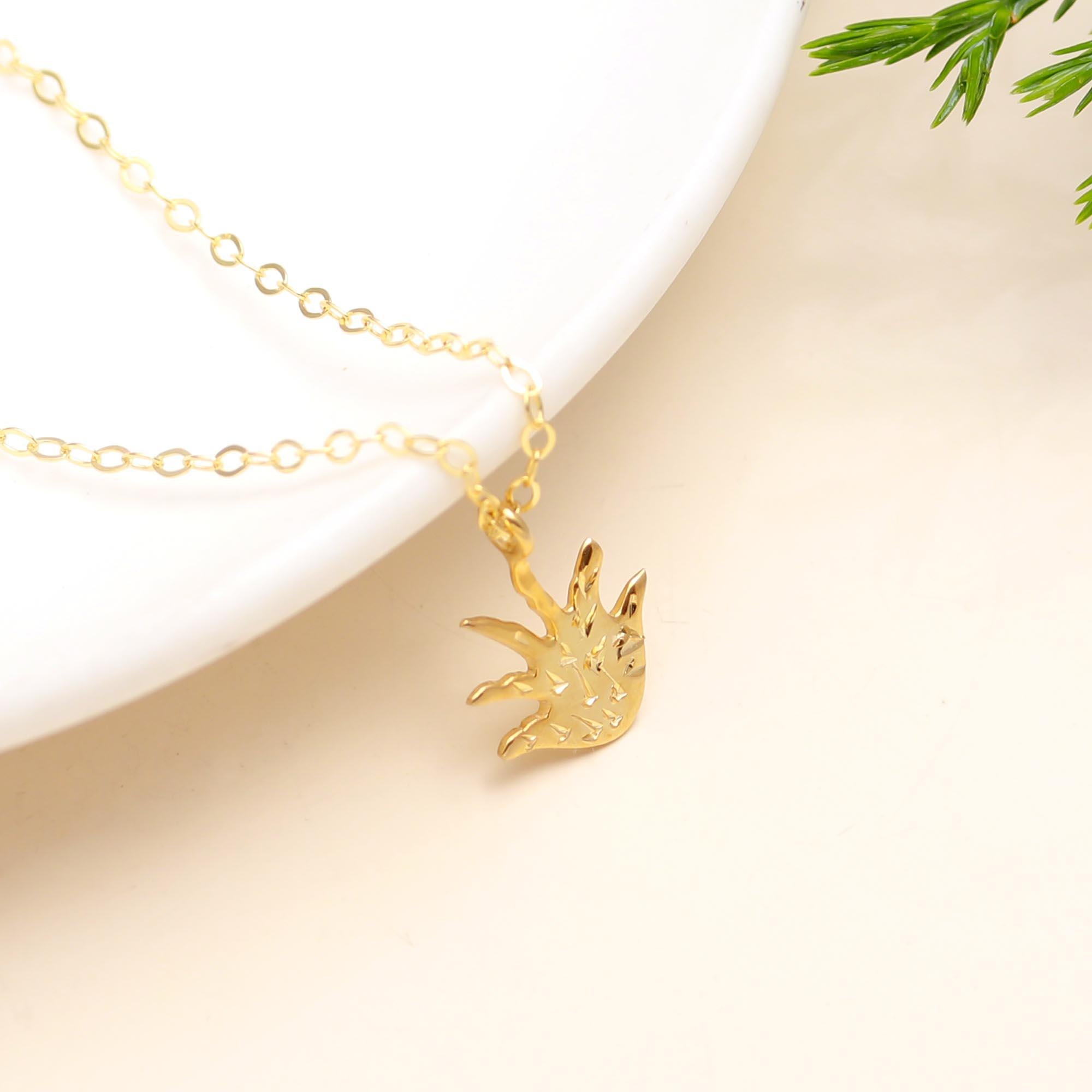 Gold necklace with a leaf-shaped pendant on a beige background