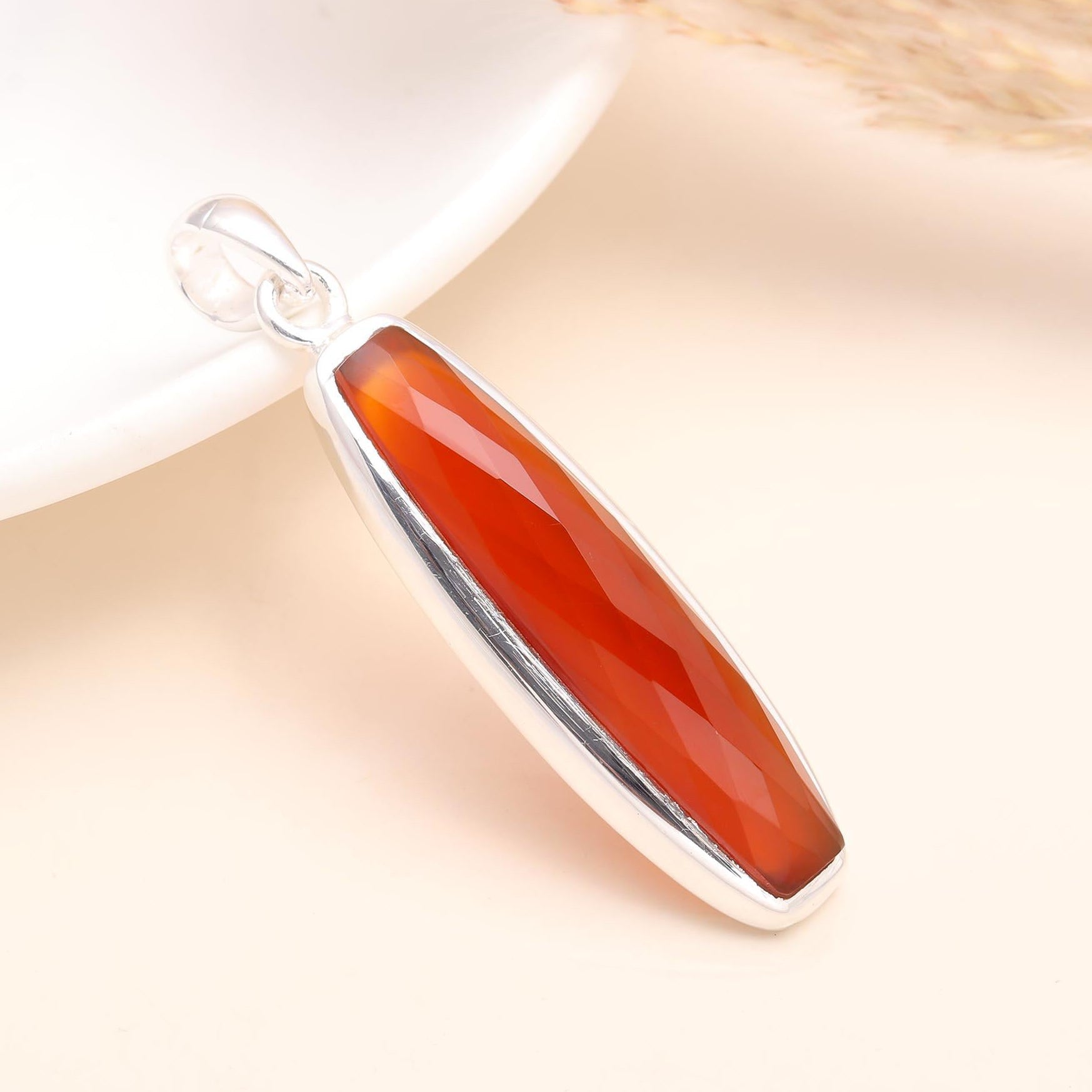 An elongated faceted carnelian gemstone pendant set in a sterling silver mounting, displayed against a light background.