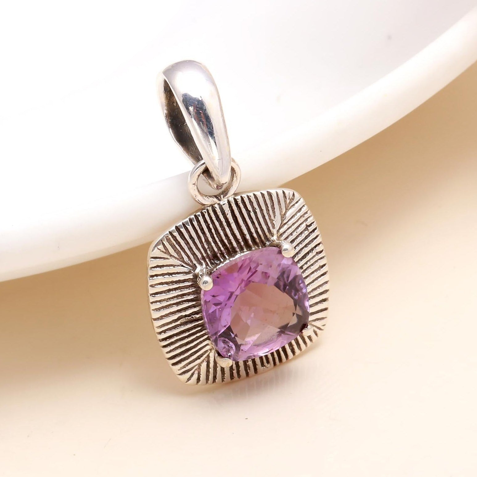 Silver pendant with a purple gemstone on a white background