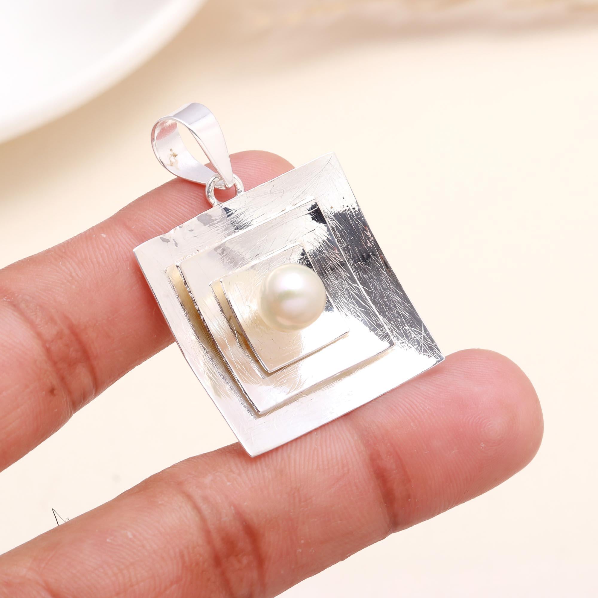 Sterling silver geometric pendant with white pearl centerpiece on a hand, modern square design.