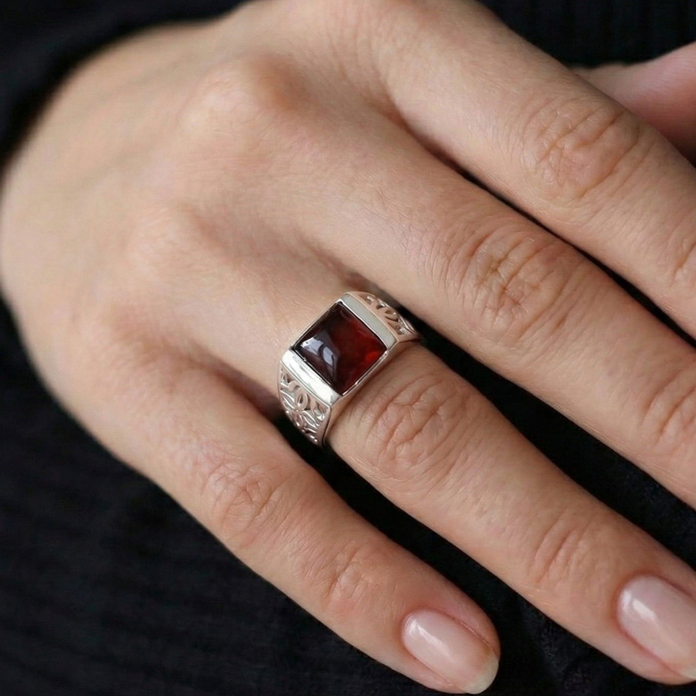 Hand wearing a ring with a red stone on a dark background