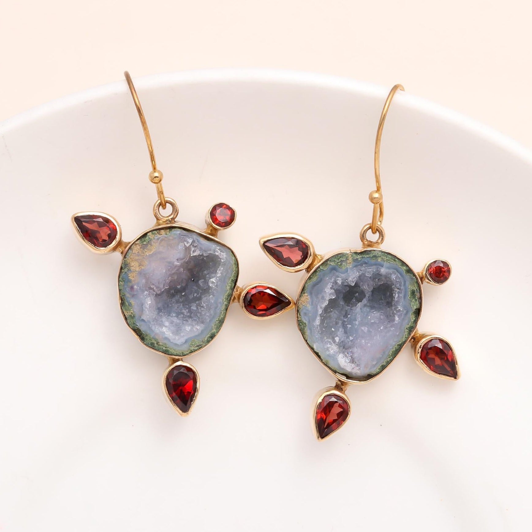 A pair of 925 Sterling Silver dangle earrings featuring raw crystal geode slices and garnet gemstones, displayed on a white plate.
