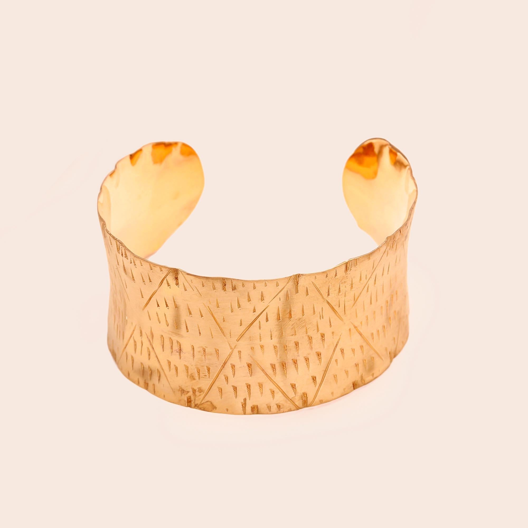 Gold textured cuff bracelet on a mannequin arm against a beige background