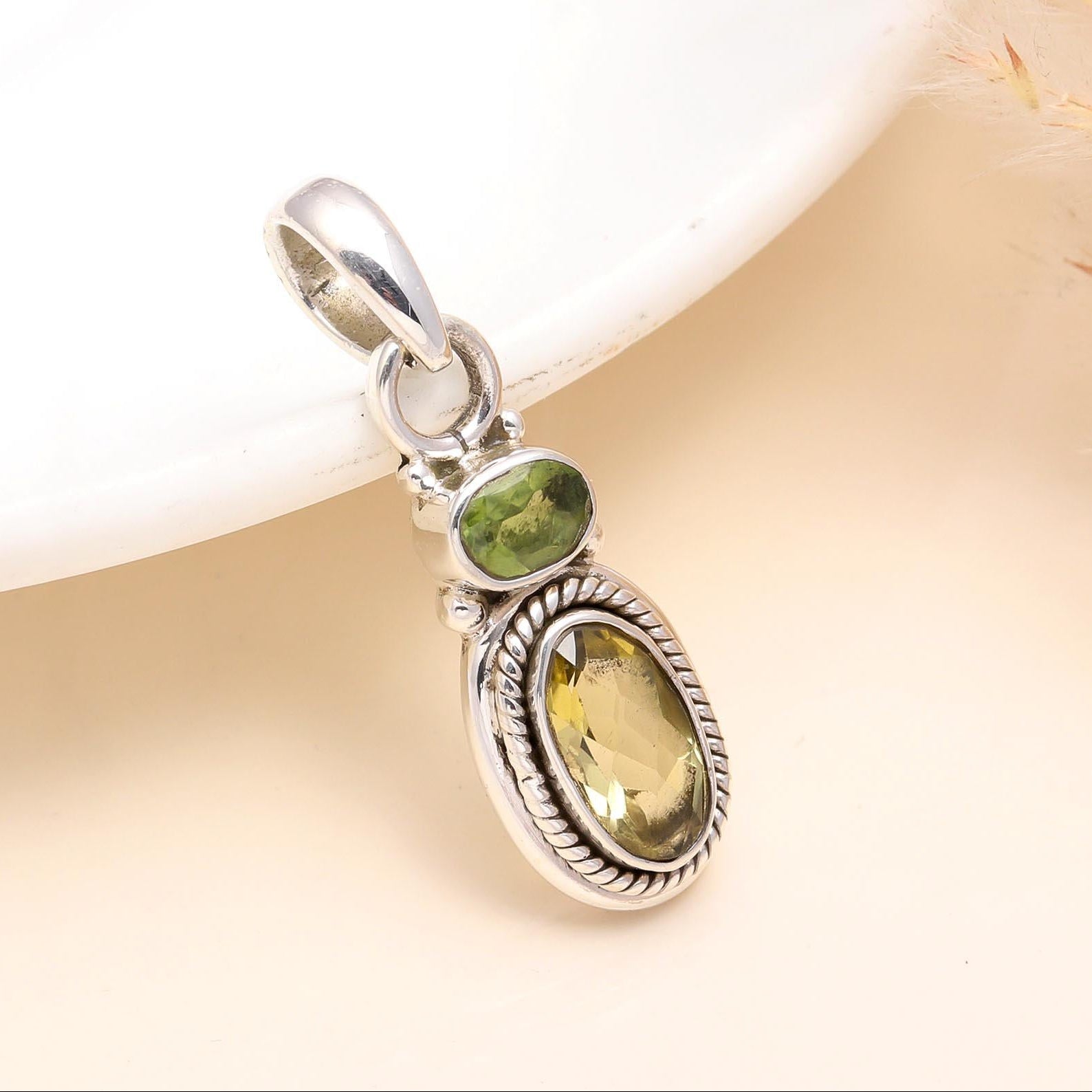 A sterling silver pendant featuring a faceted lemon quartz gemstone with a smaller peridot gemstone to the side, set against a neutral background.