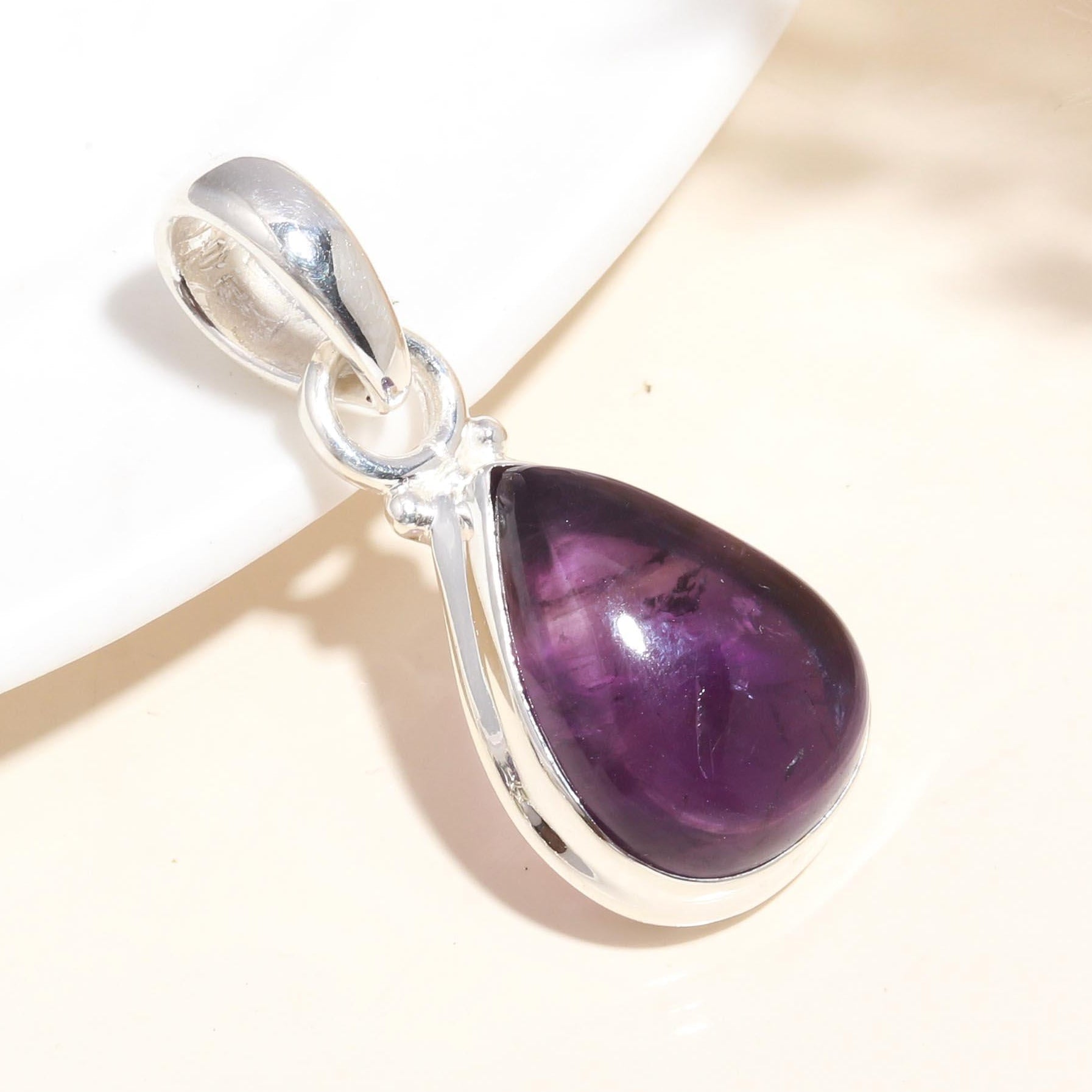 A teardrop-shaped amethyst gemstone pendant set in a silver mounting, displayed against a neutral background.