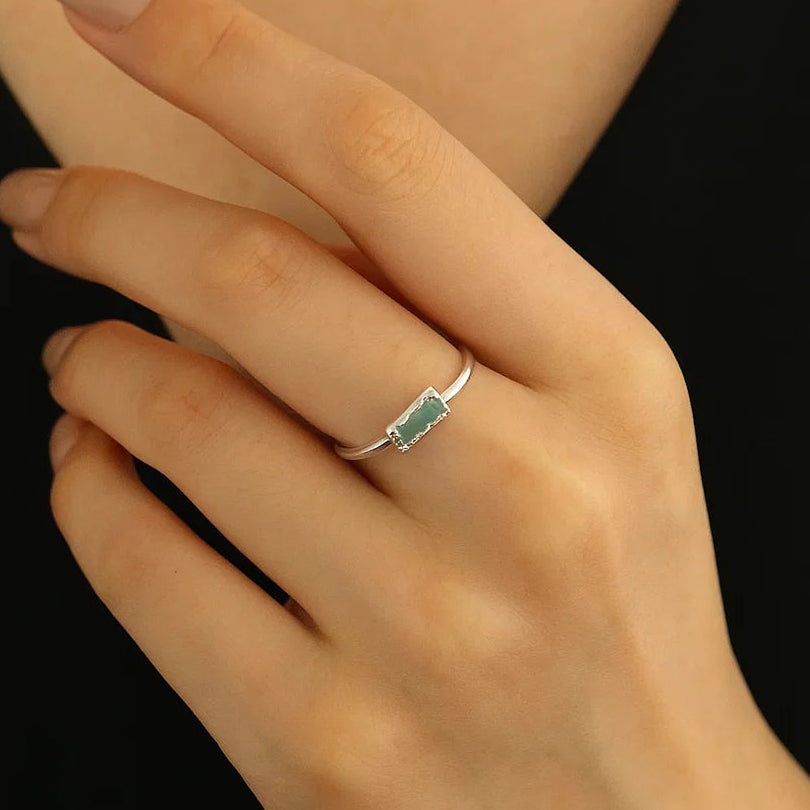 Hand wearing a silver ring with a green gemstone on a black background