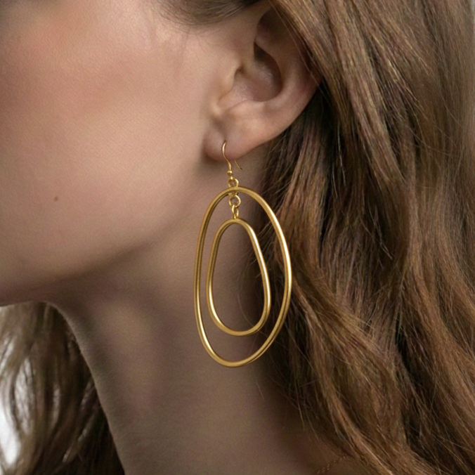 Close-up of a woman wearing gold hoop earrings with a plain background