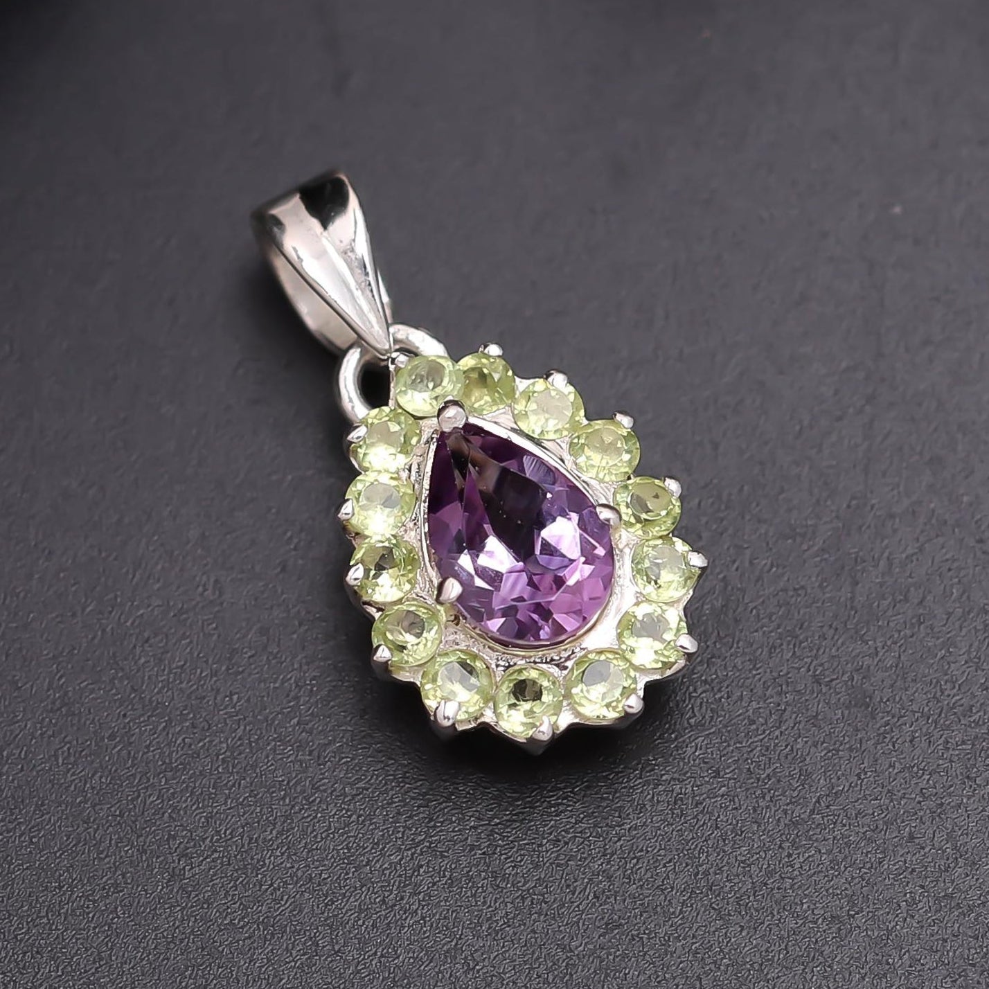 Silver pendant with a purple teardrop-shaped gemstone and green accents on a dark gray background