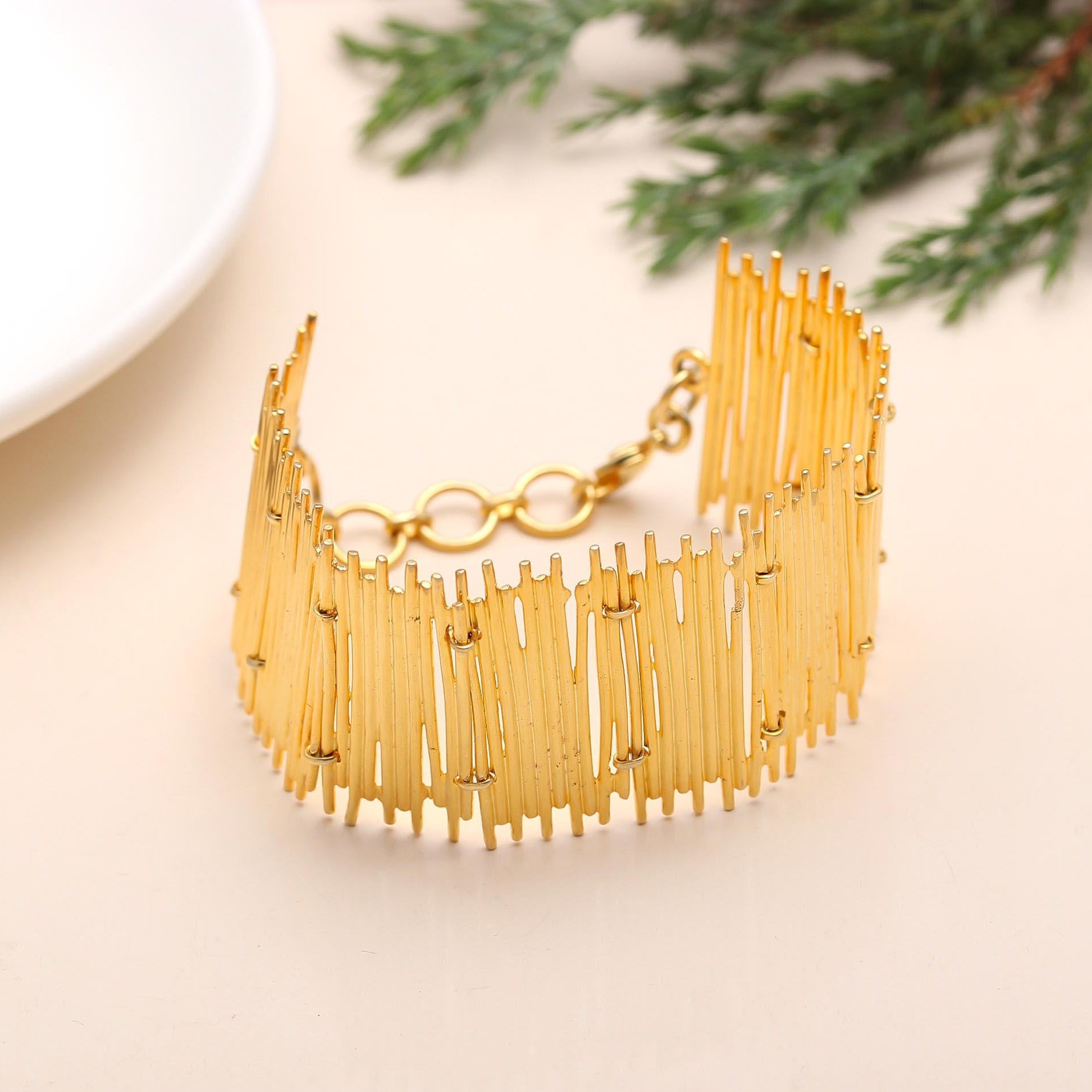 Gold bracelet on a light surface with greenery in the background