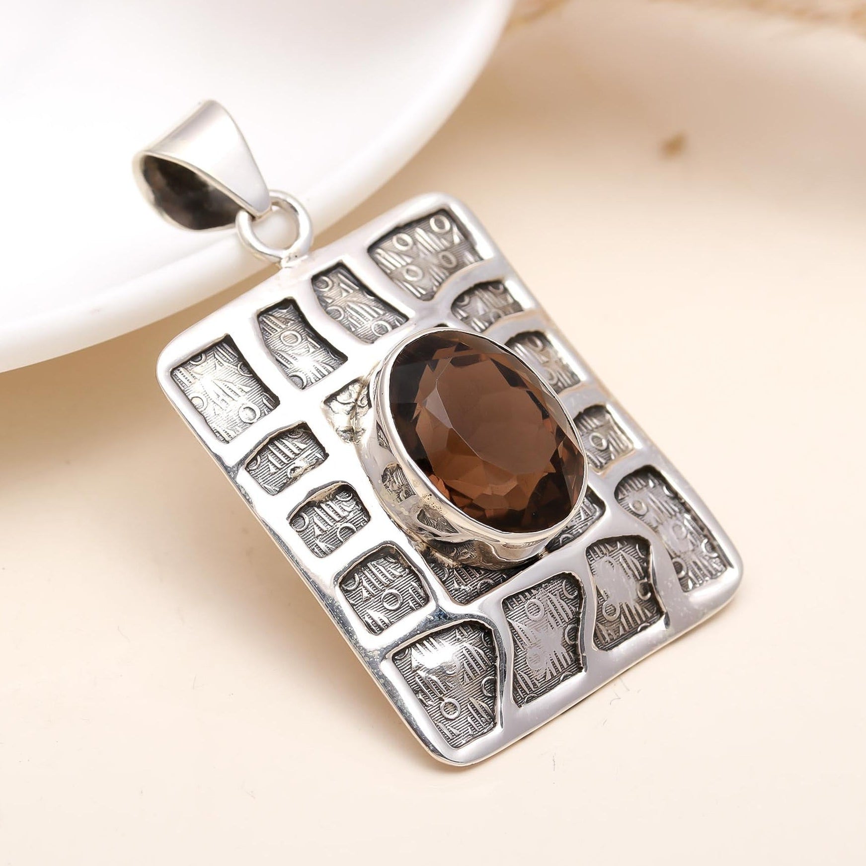 A sterling silver square box pendant with a smokey quartz gemstone in the center, displayed on a silver chain against a white background with a jute pouch.