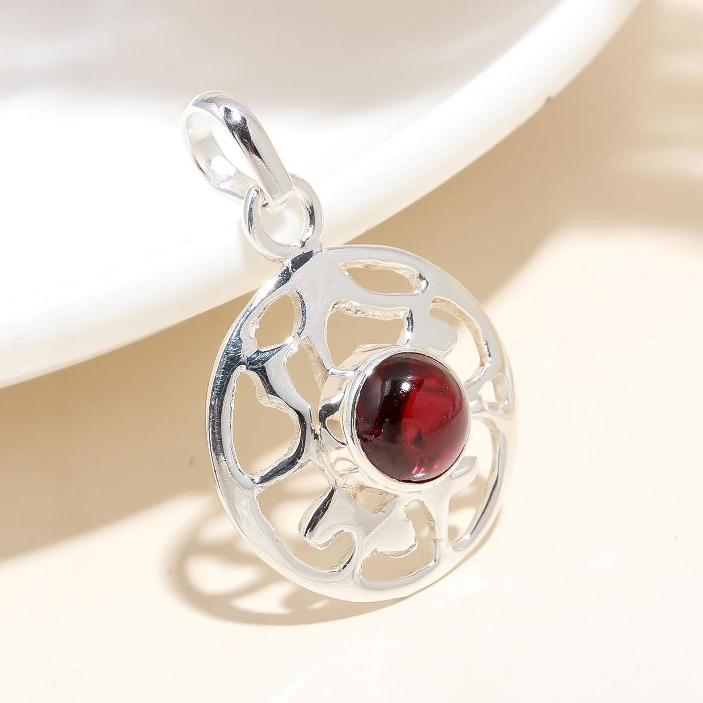 Silver pendant with a red gemstone on a beige background