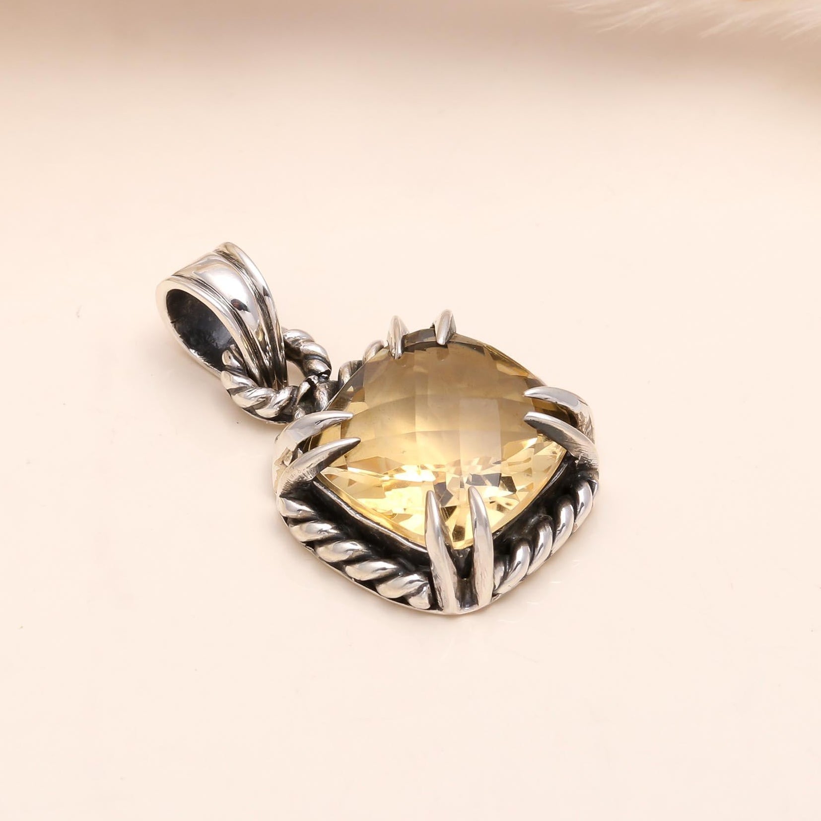 Silver pendant with a heart-shaped yellow gemstone on a beige background