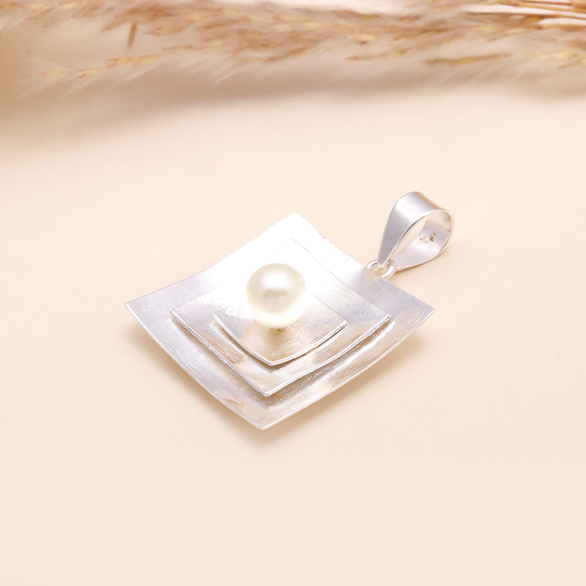 Sterling silver geometric pendant with white pearl centerpiece on a hand, modern square design.