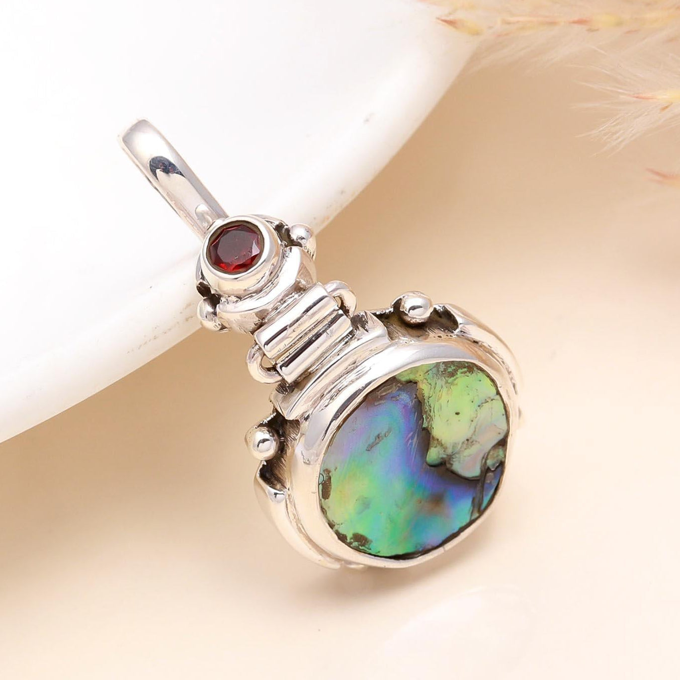 A 925 Sterling Silver pendant featuring an abalone shell with iridescent colors and a garnet gemstone, set against a white background.