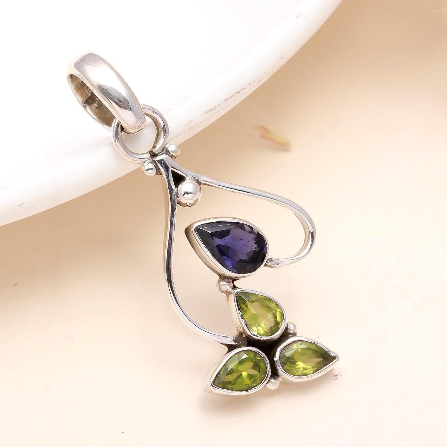 Silver pendant with purple and green gemstones on a beige background