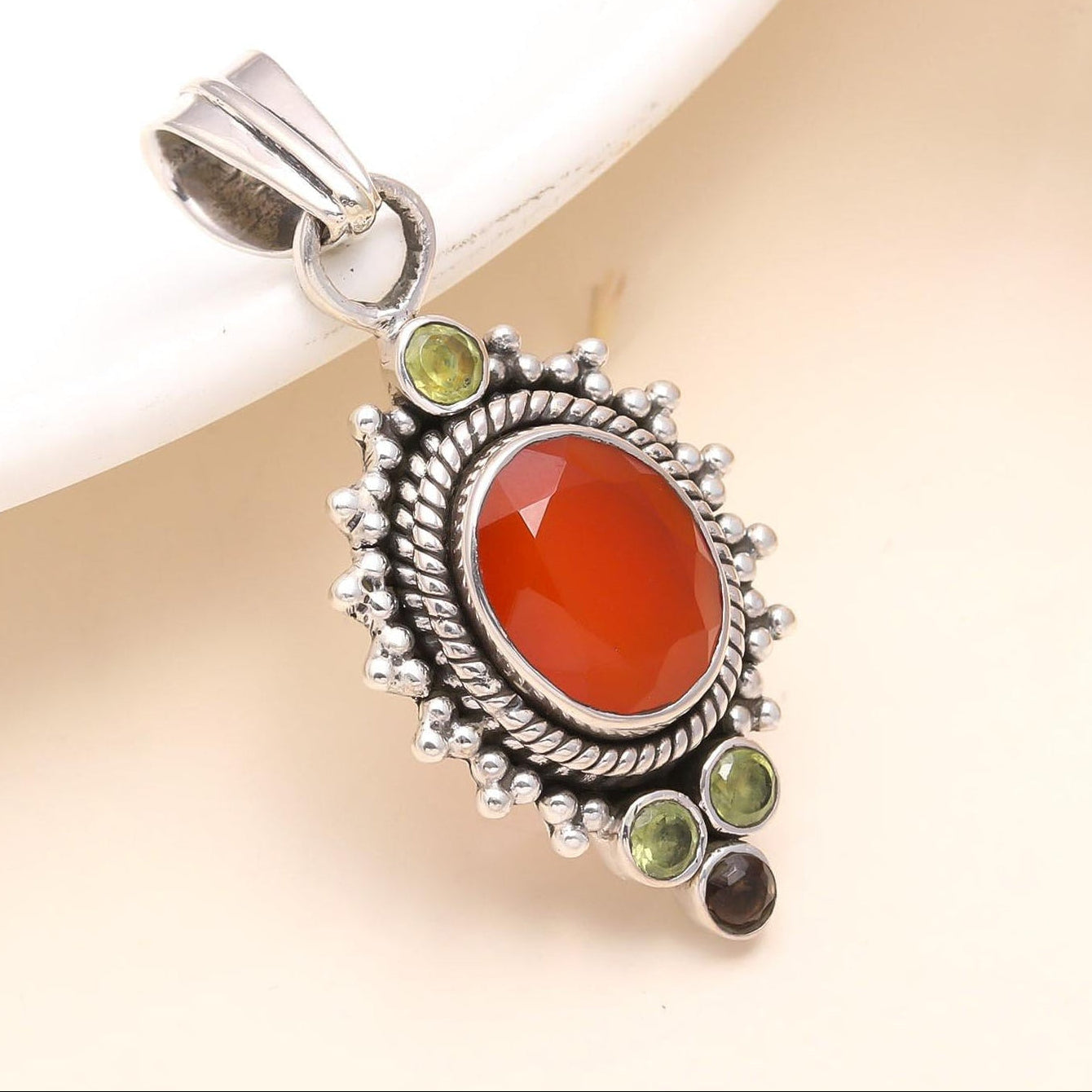 A sterling silver pendant featuring a central carnelian gemstone flanked by peridot and surrounded by small smoky quartz stones, set against a neutral background.